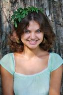 Portrait of the beautiful, smiling nymph girl, in turquoise dress, with the green leaves, near the tree, in light