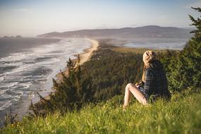 Back view of the blonde girl, sitting on the beautiful, green and yellow field, on the coast