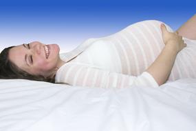 Smiling pregnant woman, laying on the white bed