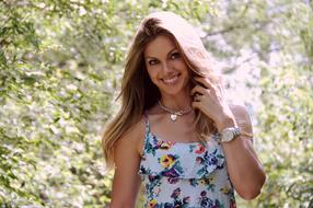 Portrait of the beautiful, smiling girl, in the colorful dress, and with the watch, among the green plants, in sunlight