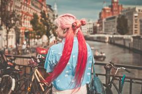 Back view of a girl with pink and red hair, near the bicycles on the iron railings, near the water