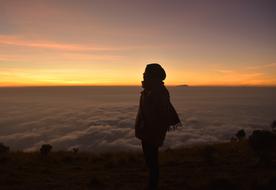 Silhouette of woman on mountain peak above clouds at dusk