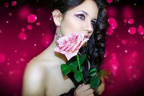 Woman with pink rose at face with make-up at pink background with petals