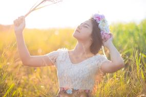 Portrait of the posing woman in colorful dress, with the colorful flower wreath, among the colorful and beautiful field in sunlight