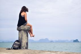 girl sitting on a concrete pillar on the embankment