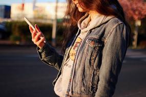 Girl in denim jacket, using smartphone, on the beautiful street