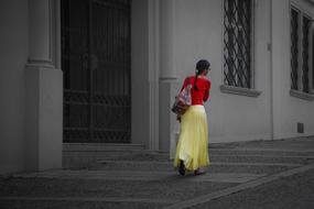 Woman in Red top and Yellow skirt walking away along wall of building