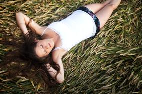 Portrait of the pregnant woman, with the closed eyes, laying on the green and yellow grass, in light