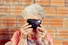 Woman with grey hair, taking photo on the camera, near the orange wall