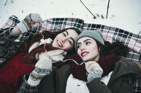 two happy Girls laying down on plaid on snow