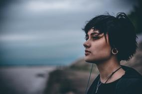 Portrait of the beautiful girl with beautiful, black short hair and earrings, on the seashore, at cloudy sky