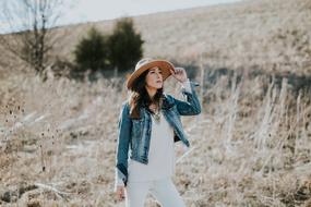 photo of a girl in a denim jacket and hat on the slope of an autumn hill