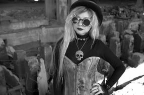 Black and white portrait of a woman in clothing, glasses and hat in style of steampunk, near the graffiti