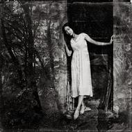 Black and white photo of the girl in white dress, posing, among the beautiful trees