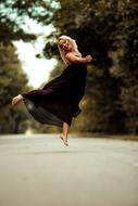 young Girl in black long dress jumping barefoot on road