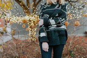 girl in a sweater near a tree with christmas lights