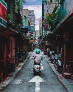 Person, riding on the motorcycle, in helmet, on the alley of Taipei, Taiwan, among the colorful buildings