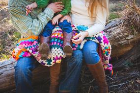 unrecognizable Man and Woman sitting with baby on log