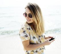 Smiling blonde girl wearing sunglasses near the water