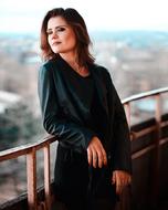 Beautiful, smiling woman with the make-up, and in dress, posing on the railing, at landscape on background