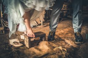 bride stands barefoot on old wooden stool beside of groom