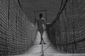 White And Black photo of Woman stands on suspension bridge