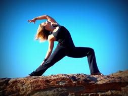 woman in yoga pose on stones against blue sky