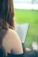 Woman with the bare shoulder, reading the book in the beautiful green garden