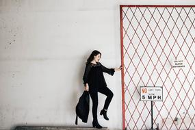 Smiling woman, with the jacket, posing near the fence and traffic signs