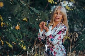 Blonde woman in colorful jacket, posing near the colorful plants