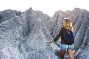 blonde girl with backpack among grey rocks