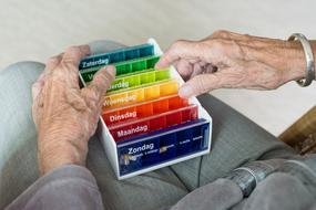 Old woman, holding the colorful pillbox with week days