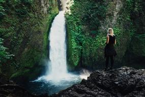 woman looking at scenic waterfall in wilderness