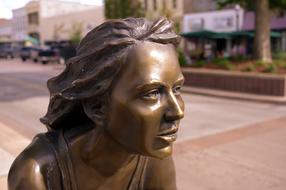 bronze sculpture of a woman on a city street on a blurred background