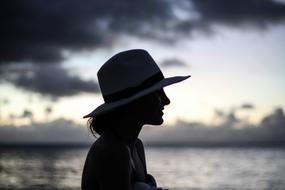 Profile portrait of the smiling woman in hat, near the beautiful water, with ripple, at colorful and beautiful sunset