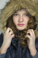 Portrait of the girl with curly hair, covered in the hood with fur