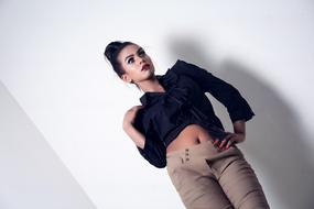 Woman in blue shirt and beige pants posing near the white wall