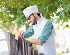 Profile portrait of a bearded man in white kurta and glasses, among the green trees in Pakistan