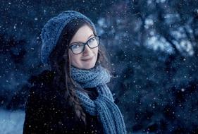 Portrait of the smiling girl with the scarf and hat, wearing glasses, among the beautiful snowy plants in winter