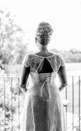 Black and white photo with the back view of the bride woman, in the patterned wedding dress, near the railing and plants