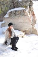 girl is sitting on a stone on the background of a snowy rock