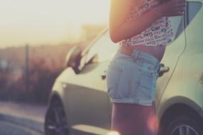 Girl in jean shorts, near the beautiful, shiny car in sunlight