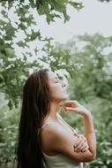 Profile portrait of a posing woman with closed eyes, among the green trees, in beautiful nature