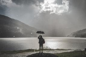 black and white photo of a girl with an umbrella near the lake