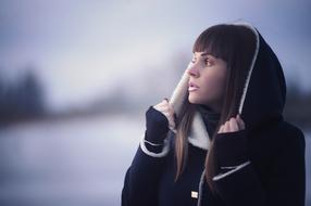photo of a brunette in a black coat with a hood on a winter field