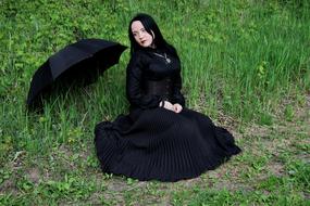 Woman in black clothing, with the necklace, with the black umbrella, on the green grass