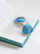 Shiny summer sunglasses on the open book, on the white surface