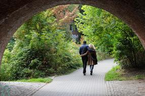 Back view from under the bridge of the walking couple, on the beautiful path, among the colorful plants