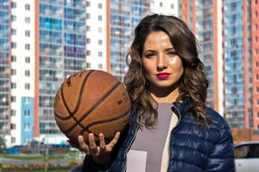 Portrait of the beautiful girl with wavy hair, with the basketball, among the colorful buildings