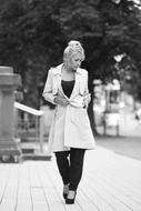 black and white photo of a walking girl in a white coat